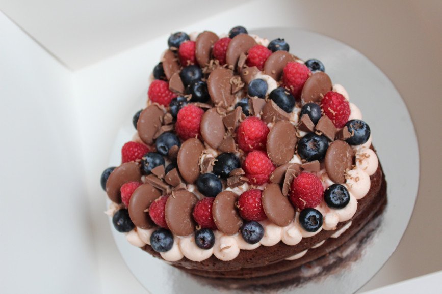 Naked chocolate heart cake topped with fresh fruit and chocolate